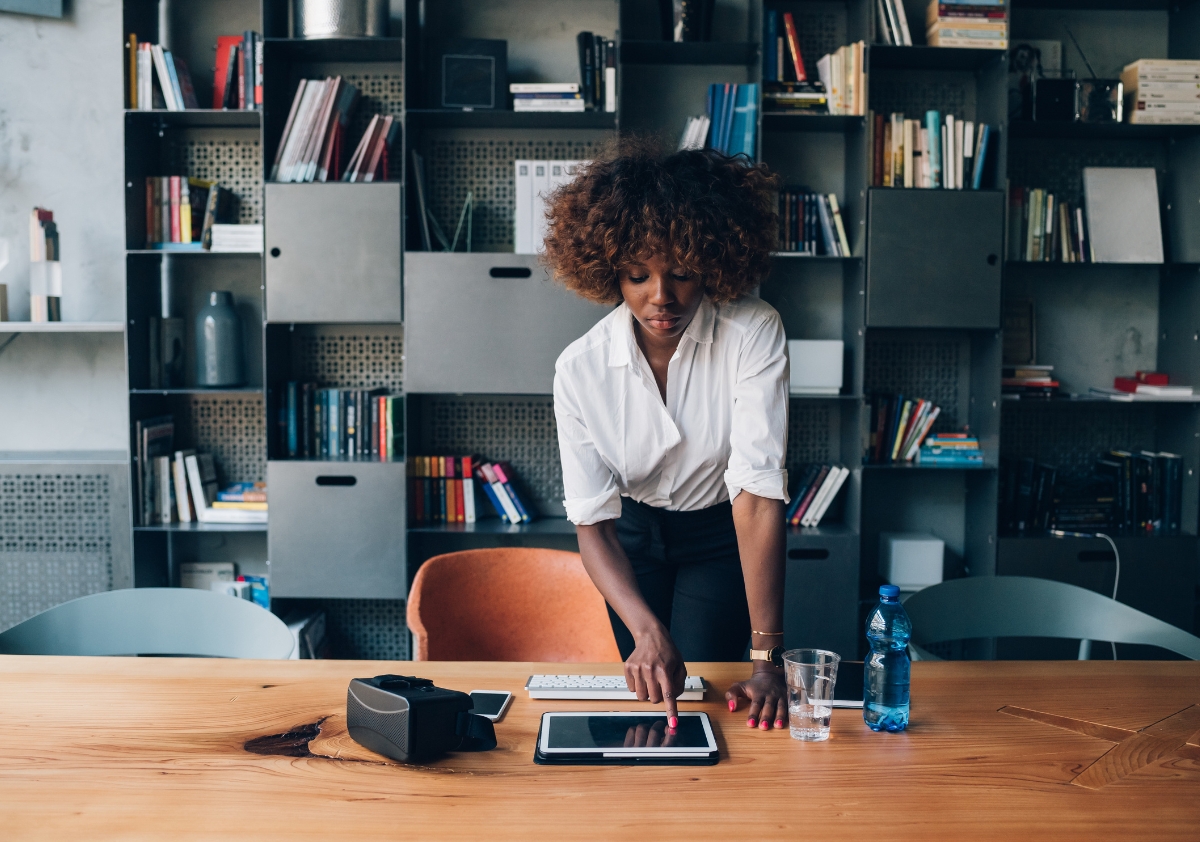 Young Black professional woman wearing a white blouse and black pencil skirts looks over her work on a tablet