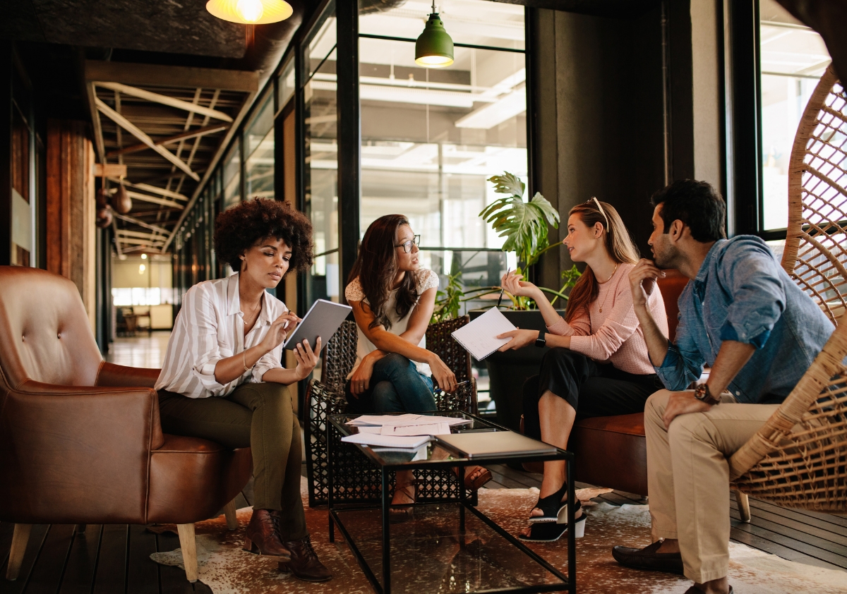 Young Black professional woman sits in a coffee shop across from her diverse team and shares her new strategy ideas