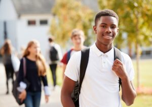 A young Black male wearing a white polo shirt and a backpack smiles after learning a company wants to acquire talent from his generation