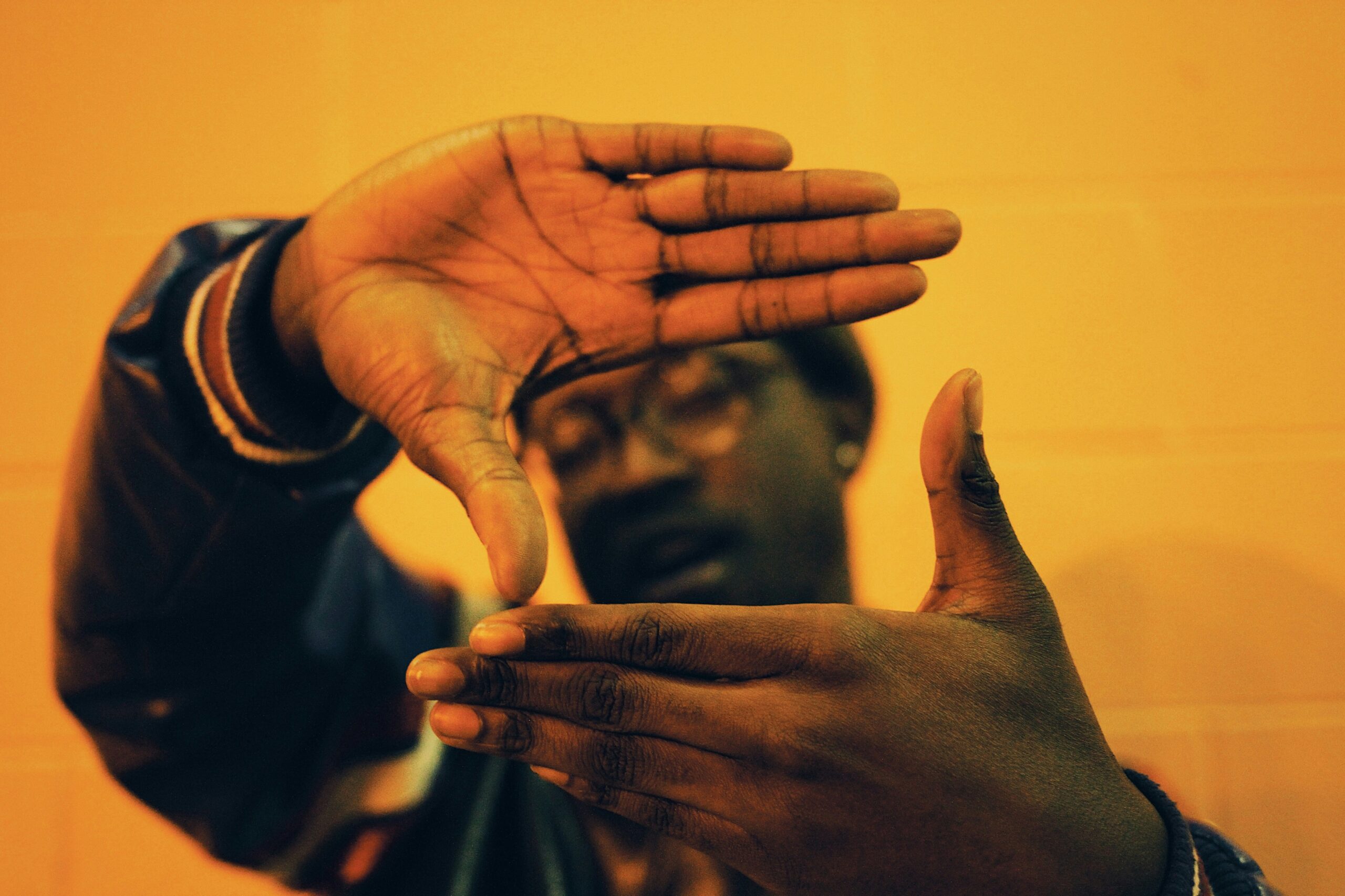 A person makes a 'frame' with their hands over a yellow backdrop. millennial stereotypes.