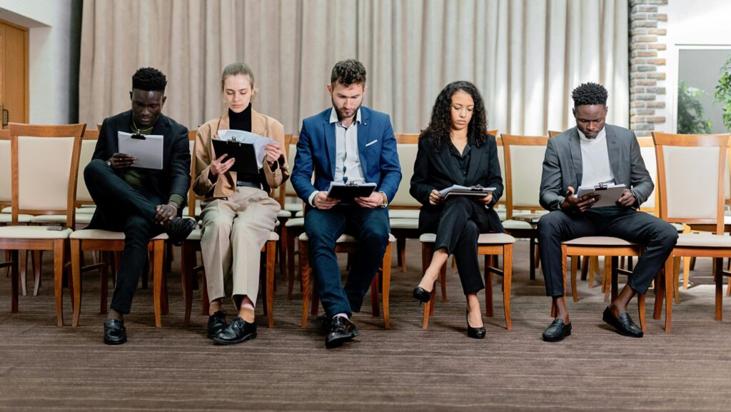 People sitting next to each other in chairs, looking at papers, waiting for job interviews. high volume hiring
